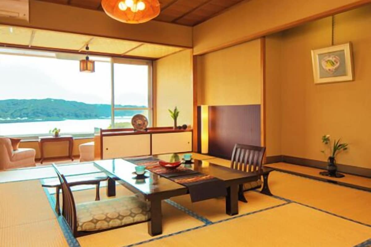 Una habitación con tatami, vista al mar, techo de madera y una mesa y sillas de estilo japonés tradicional.