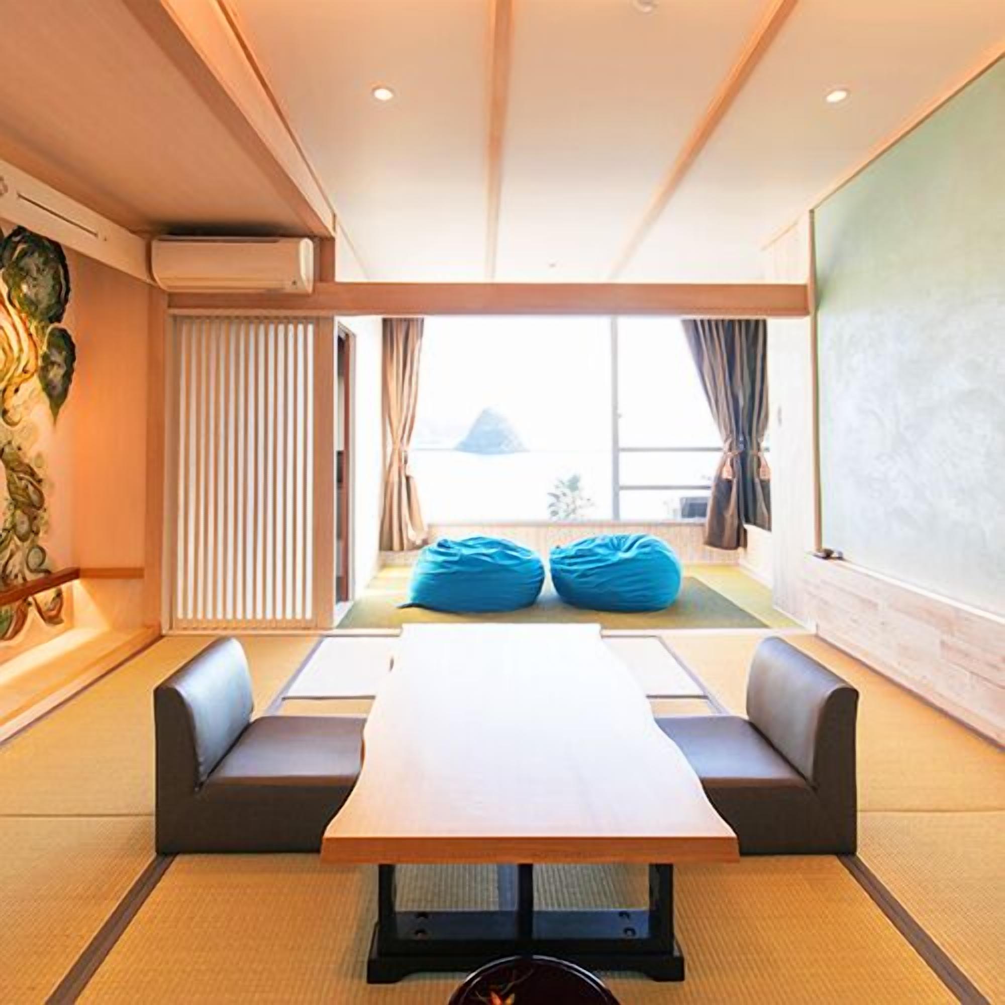 A room with a long table, two sofas, a large window, and a view of a mountain.