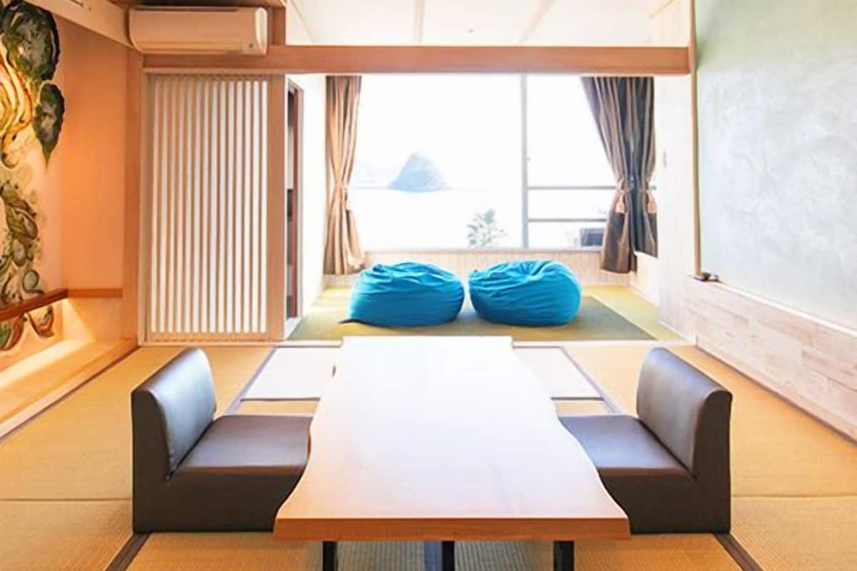 A room with a long table, two sofas, a large window, and a view of a mountain.