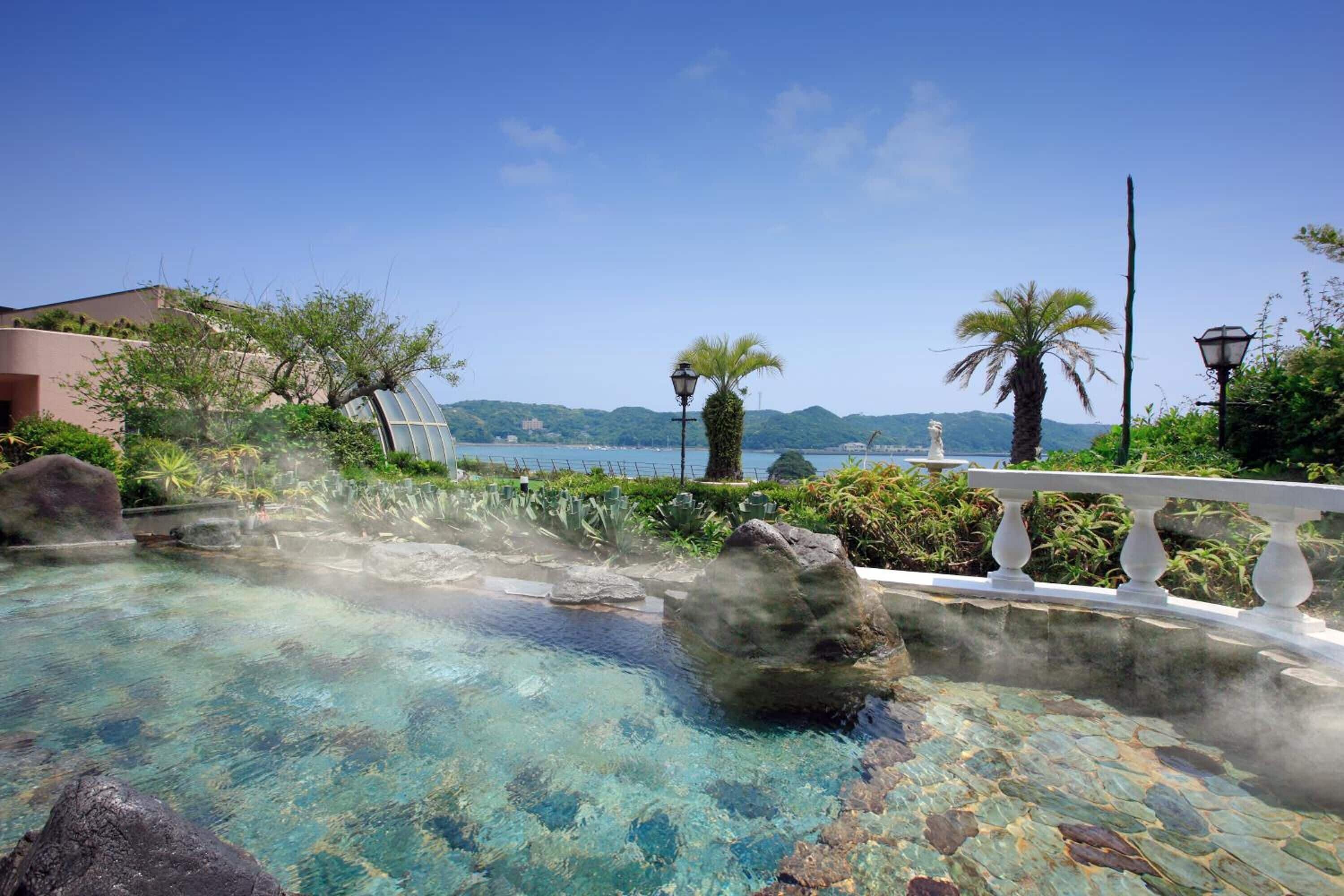 A clear pool with rocks, a white balustrade, and a view of the sea and hills.