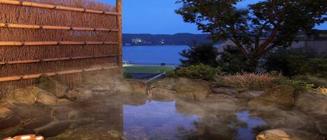 A hot spring area with a wooden fence, rocks, and a view of the water body.