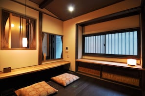 A traditional Japanese room with tatami flooring, a low wooden bench, and a large window with vertical blinds.