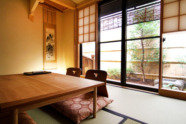 A traditional Japanese room with tatami flooring, a wooden table, and sliding doors with a view of a garden.