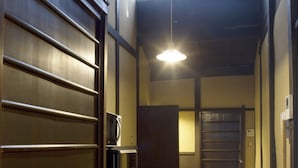A narrow hallway with a wooden floor, a metal door on the left, and a window at the end. - Demizu Machiya (Kyoto)