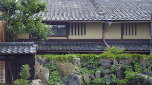 A traditional Japanese building with a tiled roof, a stone wall with greenery, and a small pond. - Demizu Machiya (Kyoto)