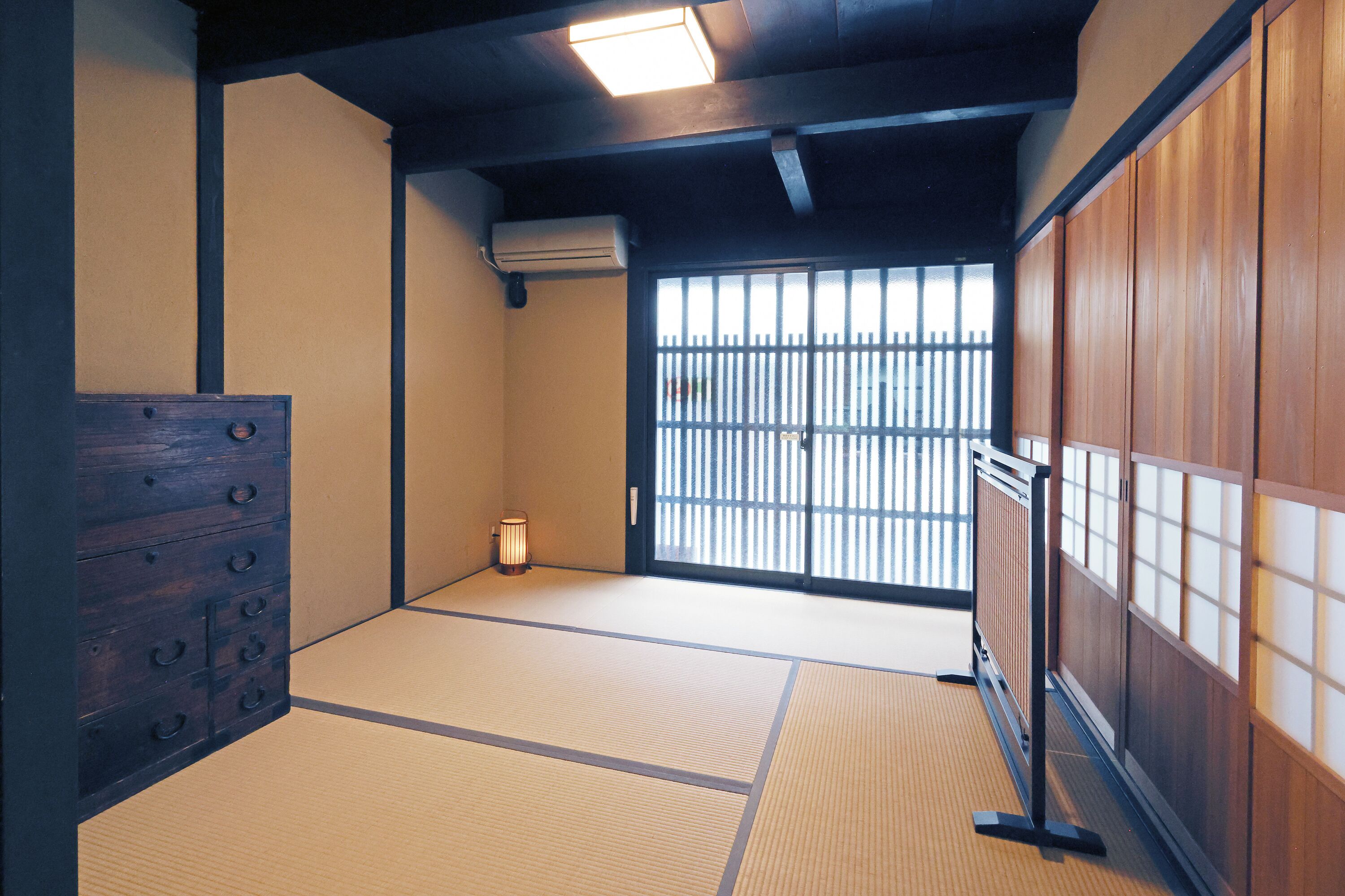 A traditional Japanese room with tatami flooring, a wooden dresser, and a sliding door leading to a balcony.