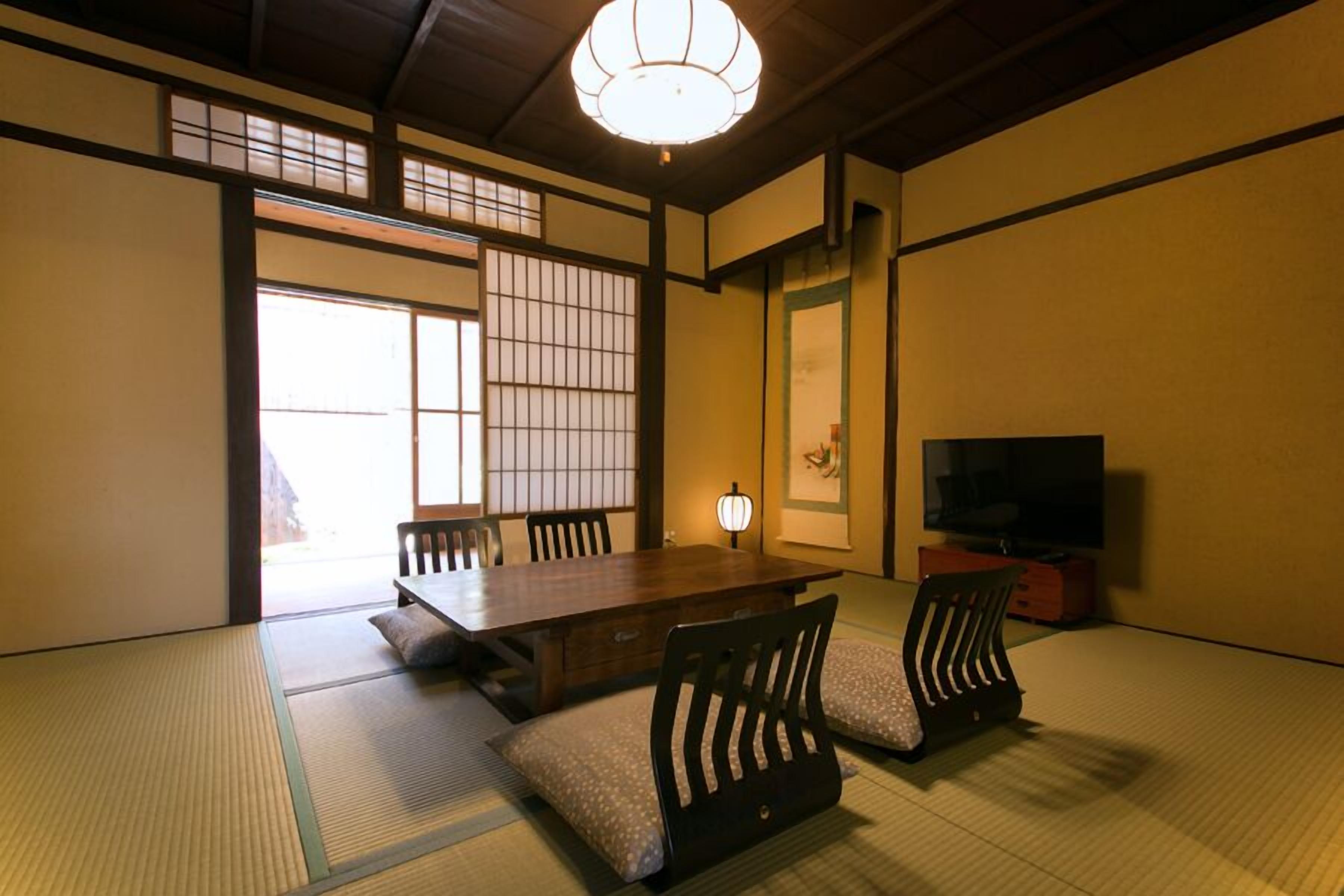 Um quarto japonês tradicional com tatames, uma mesa baixa, cadeiras, uma televisão e uma porta deslizante.