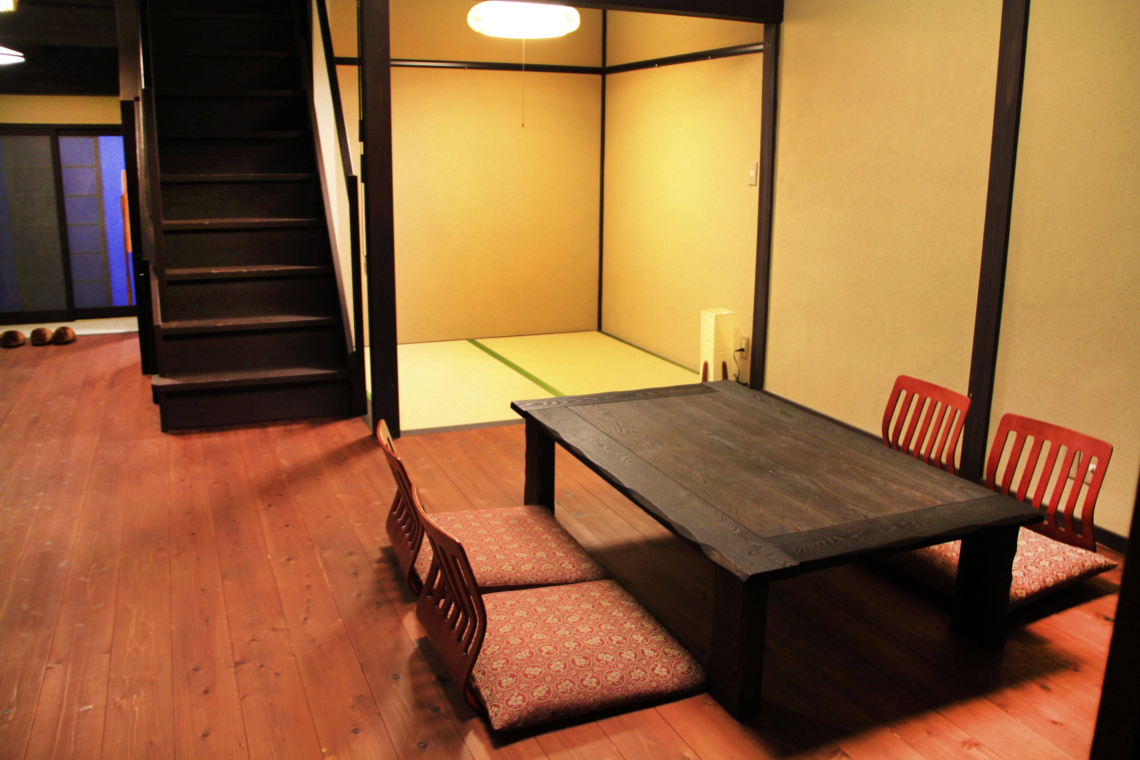 A traditional Japanese room with tatami flooring, a low table, and red chairs.