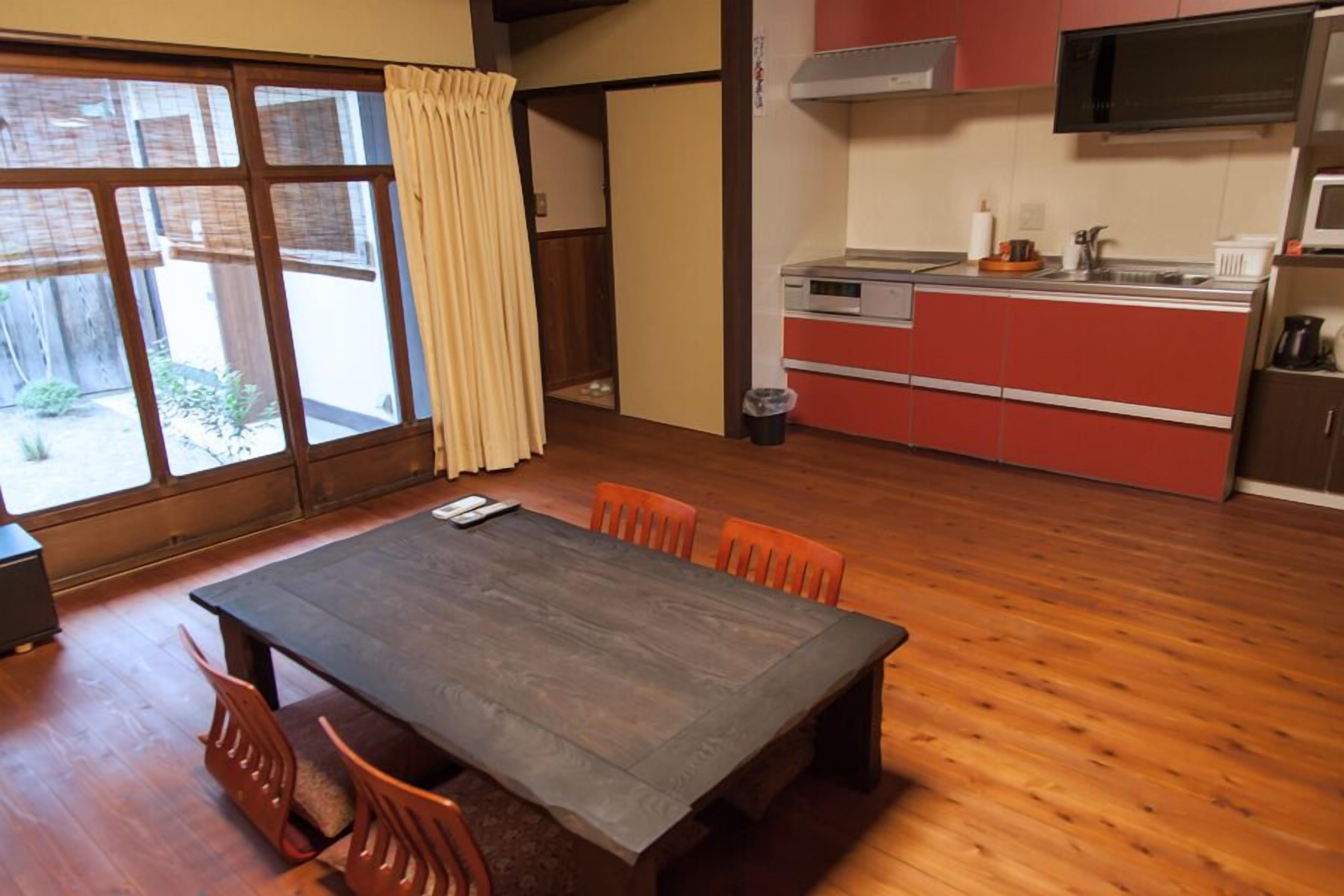 Un comedor con mesa y sillas de madera, una cocina con armarios rojos y un ventanal corredero que da a un espacio exterior.