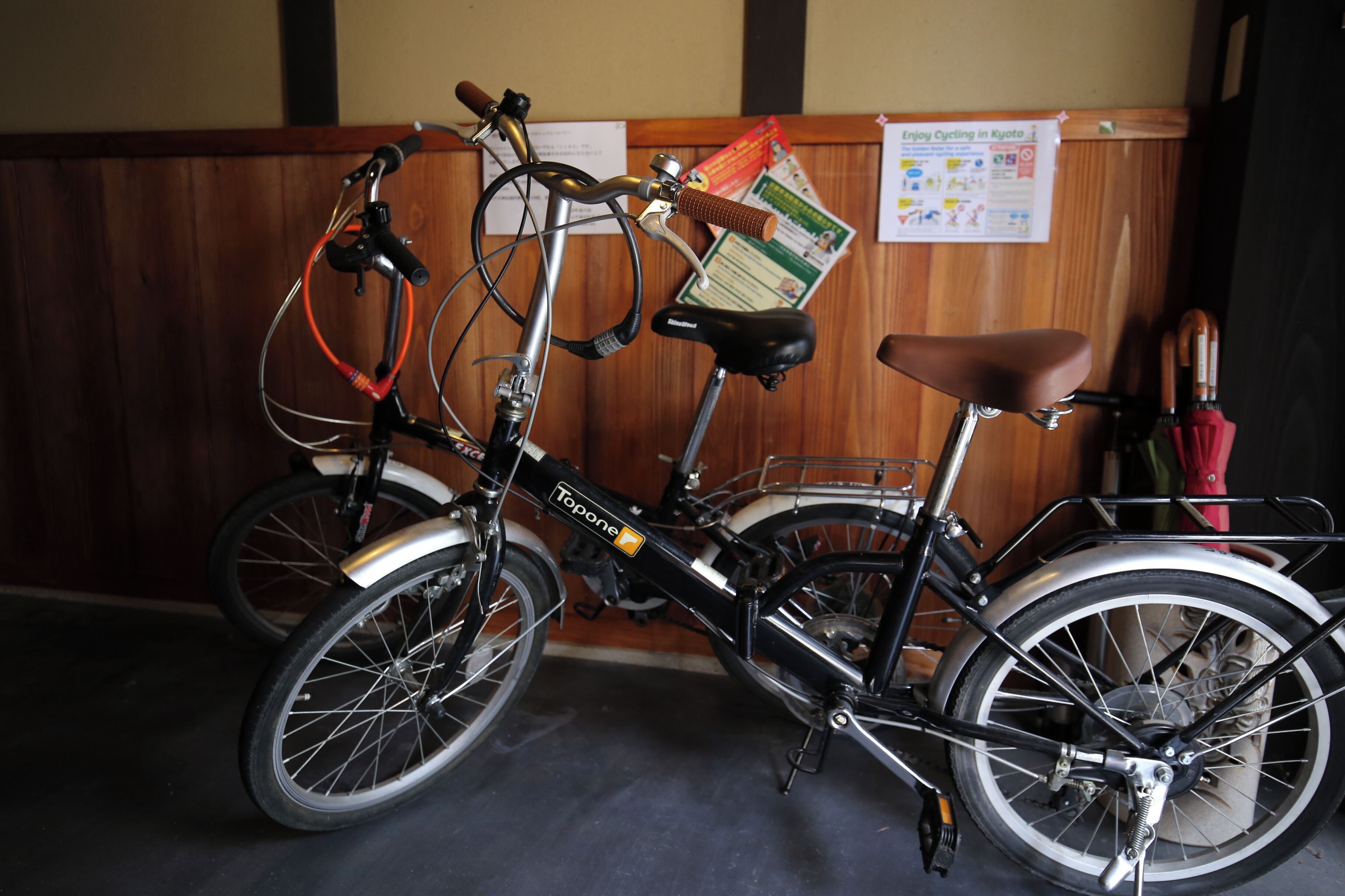 Una bicicletta con un cestino e un sellino, parcheggiata in un ambiente interno con un muro di legno e un posterello sullo sfondo.