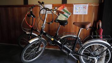 Una bicicletta con un cestino e un sellino, parcheggiata in un ambiente interno con un muro di legno e un posterello sullo sfondo.