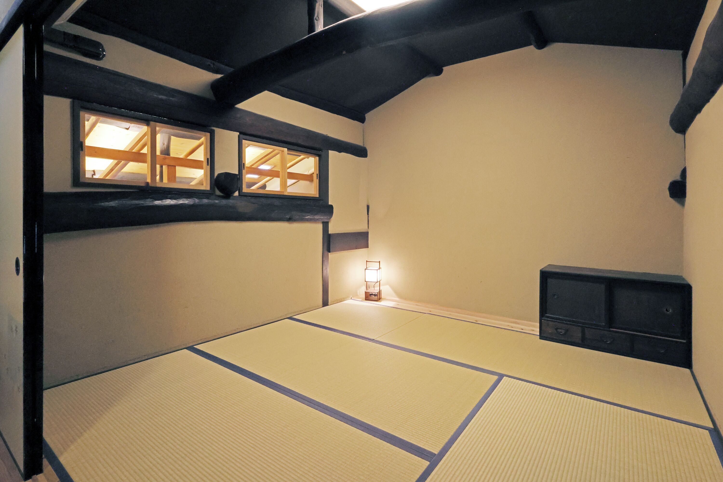 A tatami mat room with a low ceiling, wooden beams, and a small shelf.