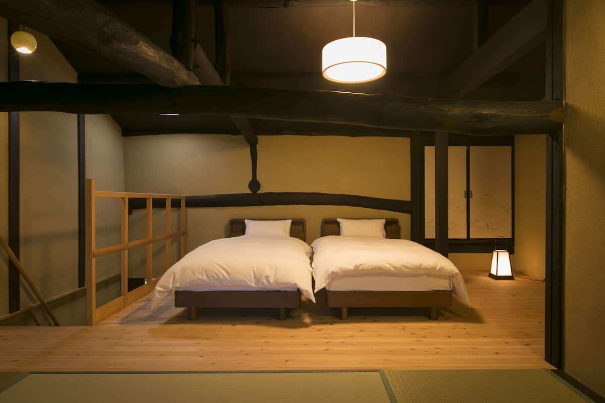 Ett traditionellt japanskt rum med två sängar av trä, ett golv täckt av tatamimattor och en hängande lampa.