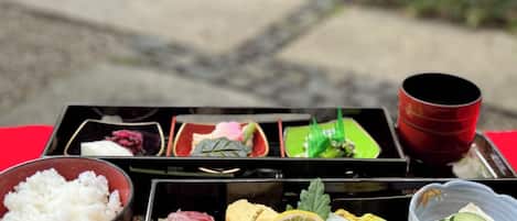 A traditional Japanese meal setup with various dishes in separate compartments, a bowl of rice, and a red cup.