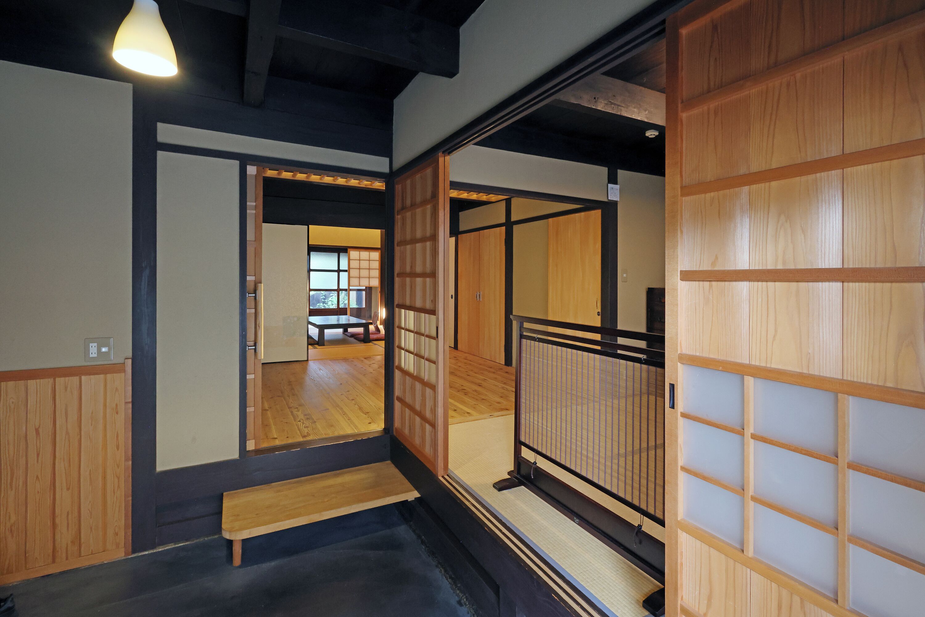 Um quarto japonês tradicional com portas deslizantes, um banco de madeira e vista para outro cômodo.