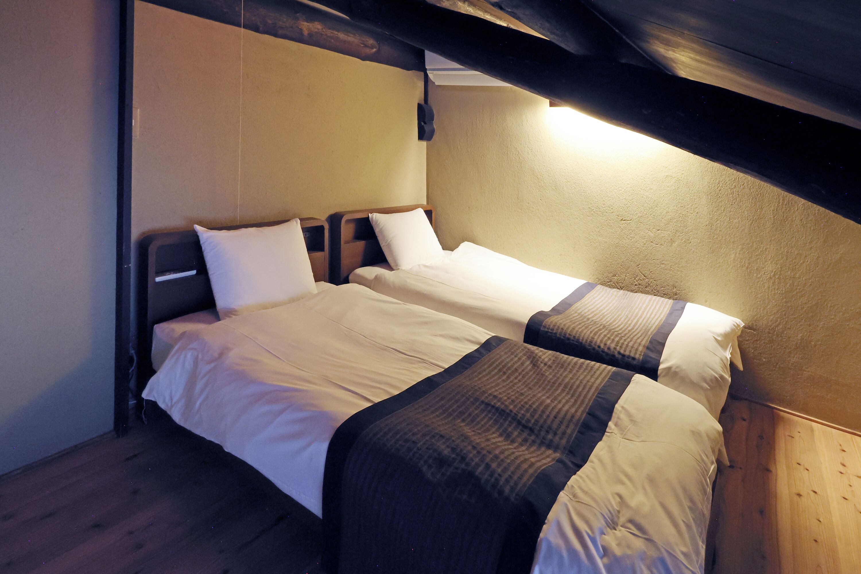 Una cama individual con cabecera de madera y colchón blanco en una habitación con paredes de madera y techo inclinado.