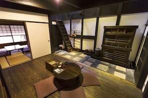 Ein traditioneller japanischer Raum mit Tatami-Böden, einem niedrigen Tisch mit Kissen, einer Leiter und einer Schiebetür.