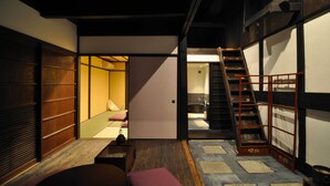 Una habitación japonesa tradicional con suelo de tatami, una cama baja de madera, una puerta corredera y una escalera de madera.