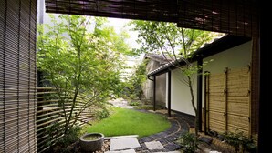 Un jardín japonés tradicional con senderos de piedra, un pequeño césped, cercas de bambú y un edificio con tejado de tejas.