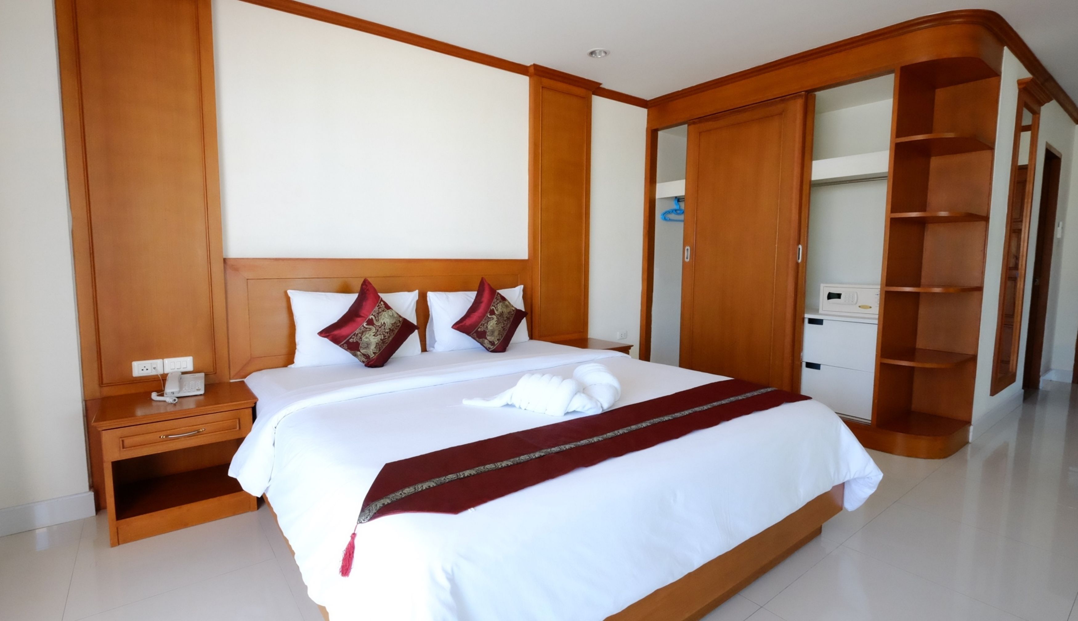 Une chambre d’hôtel avec un grand lit, une tête de lit en bois, des tables de chevet, une armoire et une salle de bain visible à travers une porte ouverte.