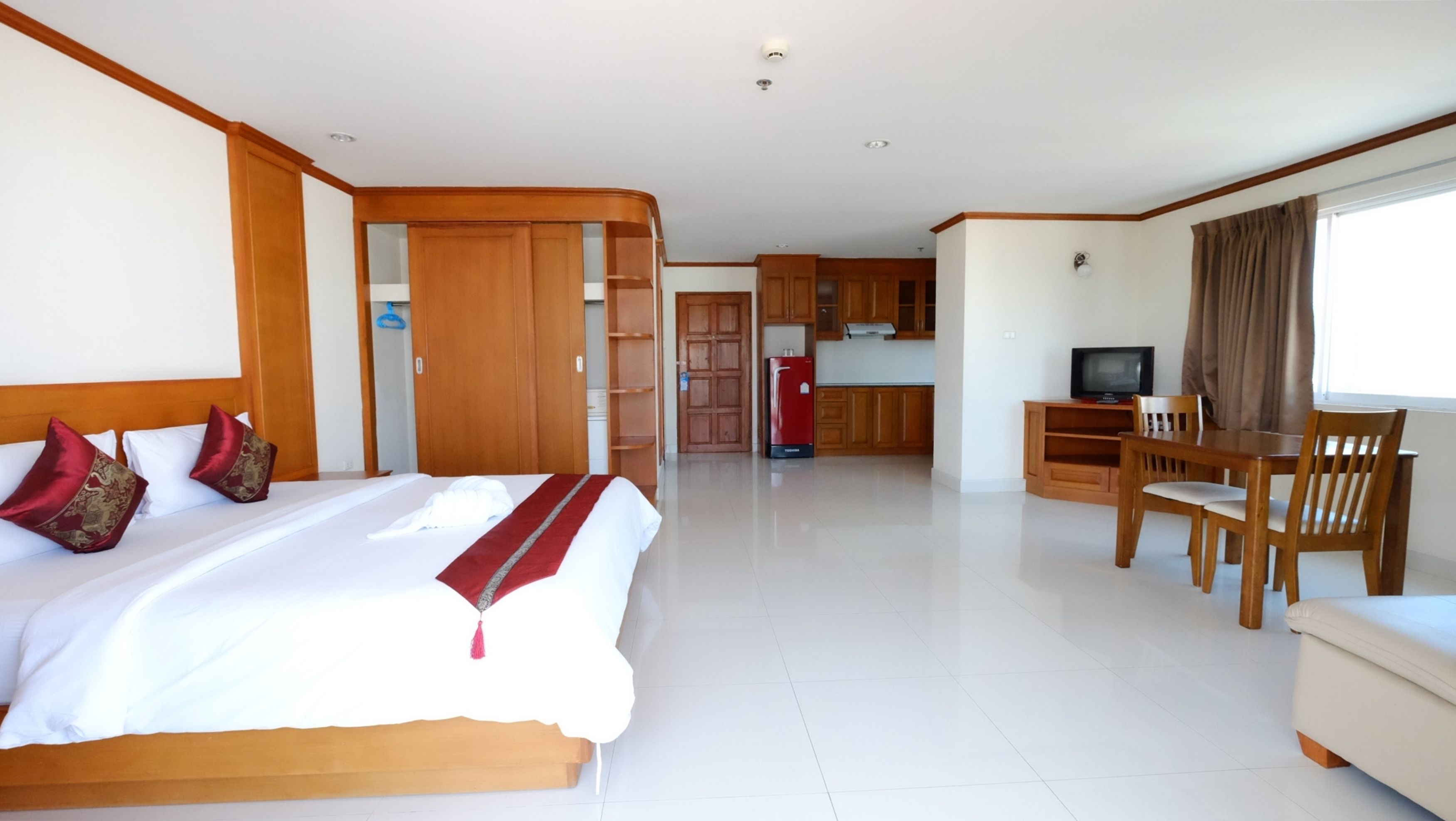 A hotel room with a bed, a desk, a chair, a television, and a kitchenette.