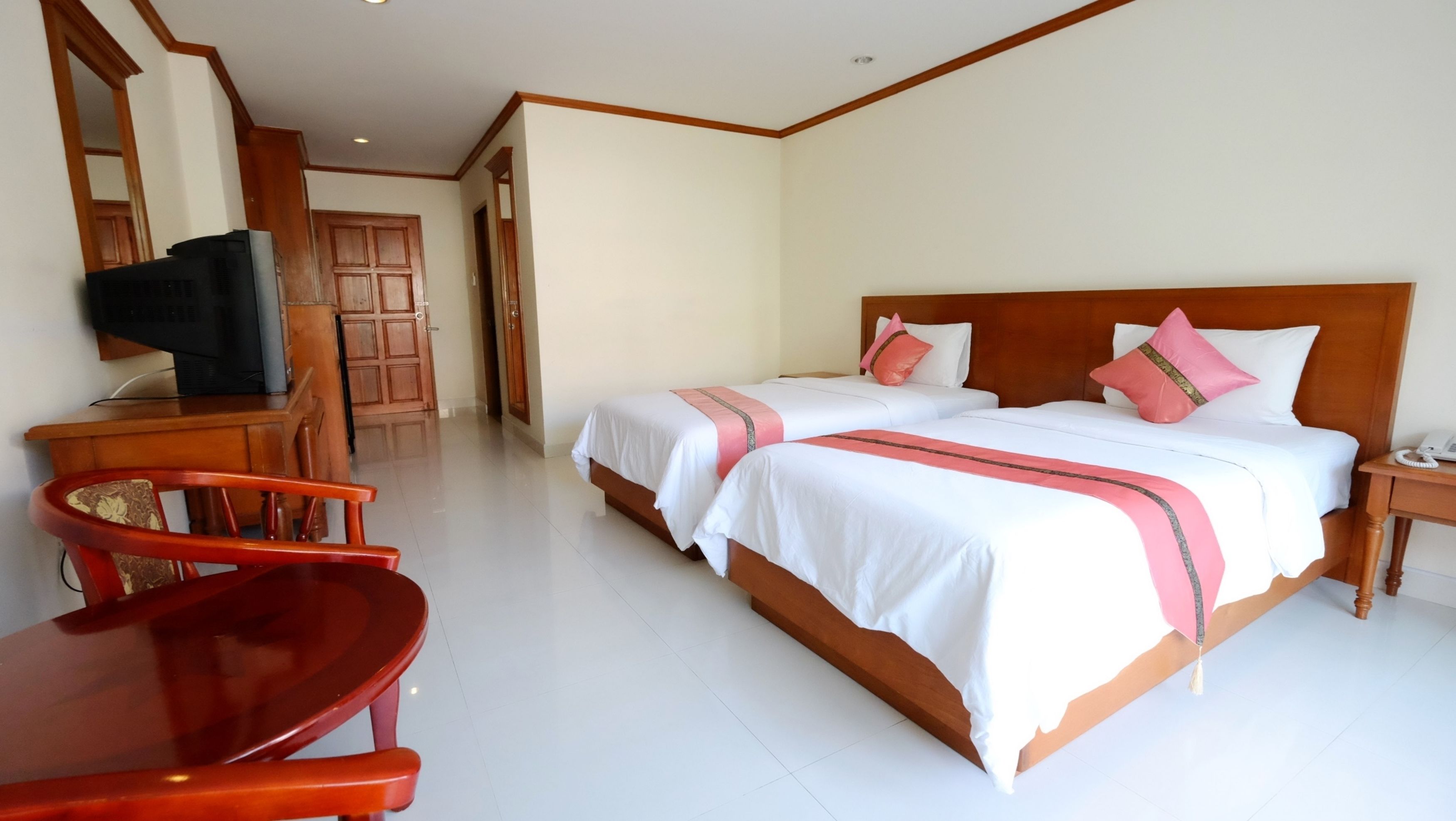 A hotel room with two beds, a wooden headboard, a desk with a chair, a television, and a phone on a nightstand.