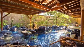 A hot spring area with a wooden roof and rocks around the pool. - Ryokan Tokiichiyu (Minamiizu)