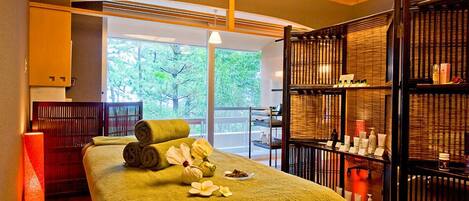 A spa room with a massage table, towels, flowers, and shelves with bottles.