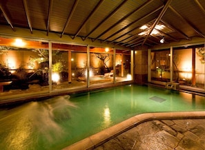 Una piscina interior con borde de piedra, paredes de cristal e iluminación cálida.