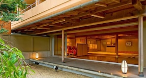 Un hotel moderno con un área exterior cubierta, una recepción y una habitación visible con una cama y una silla roja.