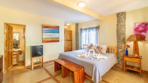Ein Schlafzimmer mit Bett, Holzbank, Fernseher und einer Steinwand.