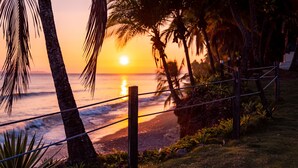 Eine Strandansicht bei Sonnenuntergang, mit Palmen und einem Seilzaun.