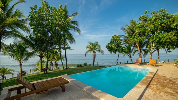 Ein Pool mit Holzterrasse, umgeben von Palmen und Blick aufs Meer.