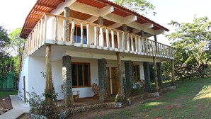 Ein zweistöckiges Haus mit Balkon, Steinsäulen und Garten.