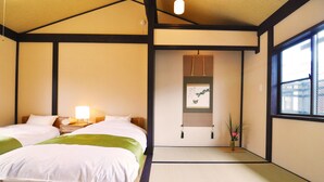 Ein traditionelles japanisches Schlafzimmer mit Tatami-Böden, zwei Betten, einem Nachttisch mit Lampe und einem Fenster mit Blick ins Freie.
