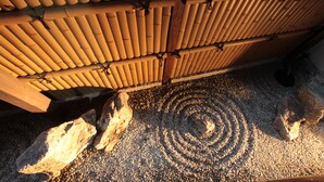 Una estructura tradicional japonesa con techo de madera sostenido por cañas de bambú, suelo de grava y grandes rocas.