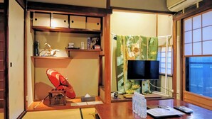 Una habitación japonesa tradicional con suelo de tatami, un futón, una televisión y una puerta corredera con cortina floral.