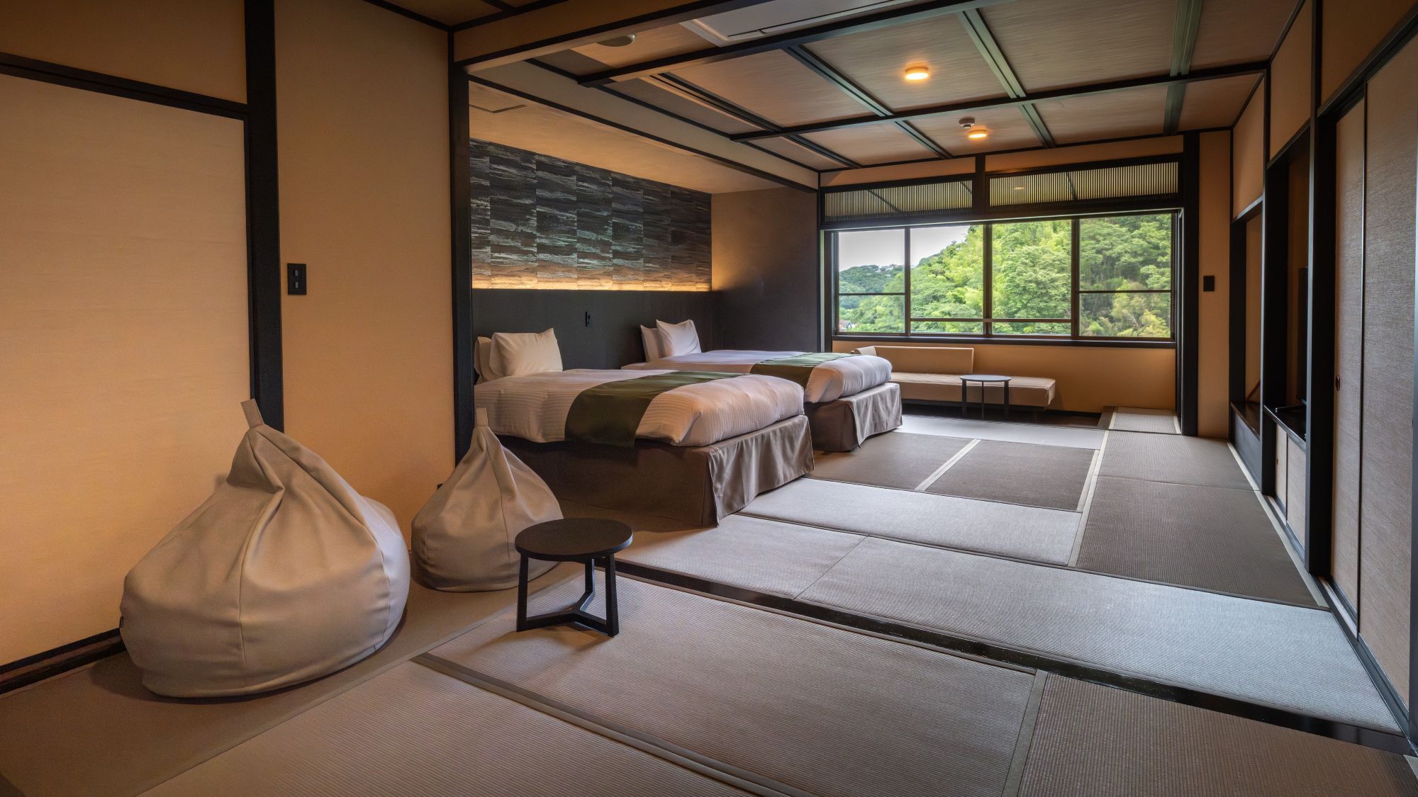 A modern hotel room with tatami mats, a bed, a seating area, and a view of greenery.