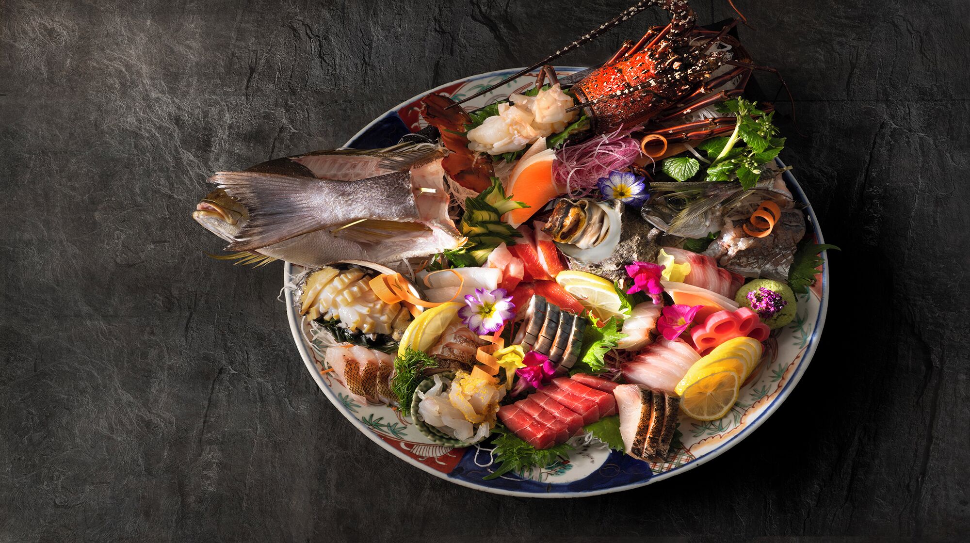 Un piatto di mare con diversi tipi di pesce e frutti di mare, tra cui gamberi, capesante e uova di pesce, disposto su un piatto decorativo.