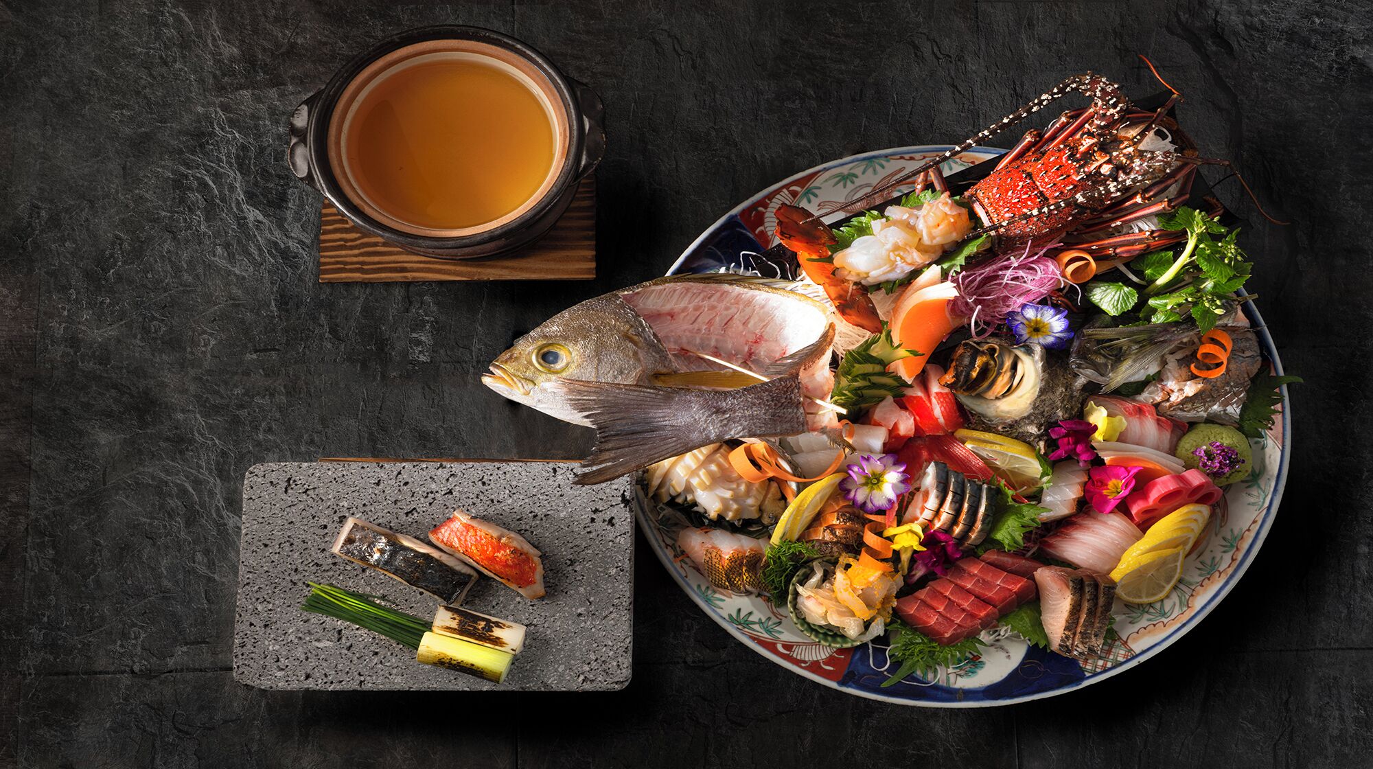 Un plateau de fruits de mer comprenant divers mets, notamment un homard, du poisson et d’autres fruits de mer, accompagné d’une tasse de thé.