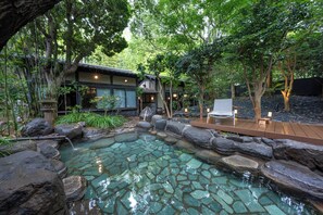 Un bâtiment de style japonais traditionnel, doté d'un bassin à carpes koï, d'une terrasse en bois et entouré de verdure.