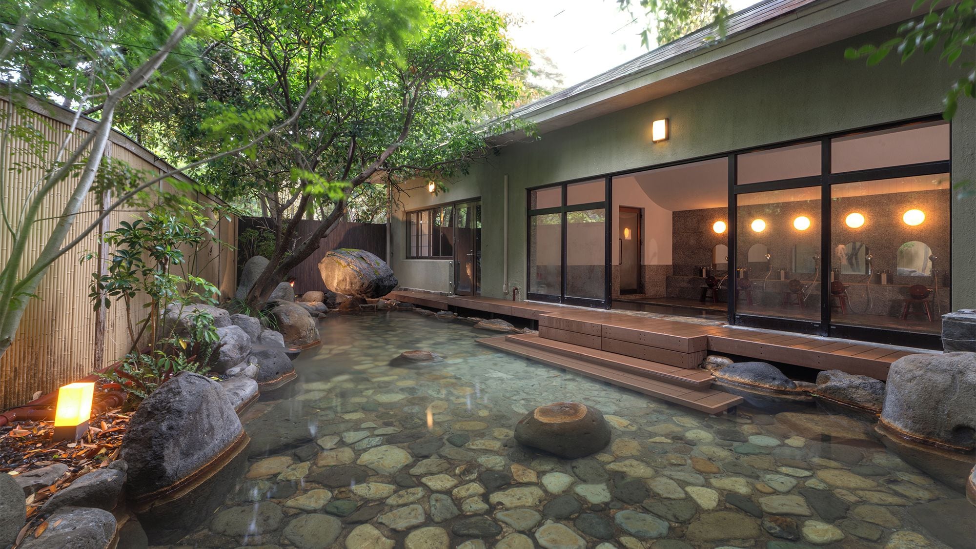 A tranquil outdoor spa area with a stone pool, wooden deck, and a building with large windows.