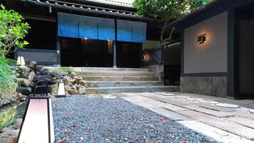 A traditional Japanese garden with a koi pond, stone steps, and a blue awning over a building entrance.