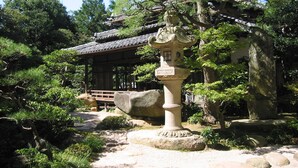 Un jardin japonais traditionnel agrémenté d’une lanterne en pierre, d’un pavillon en bois et d’un sentier de pierres.
