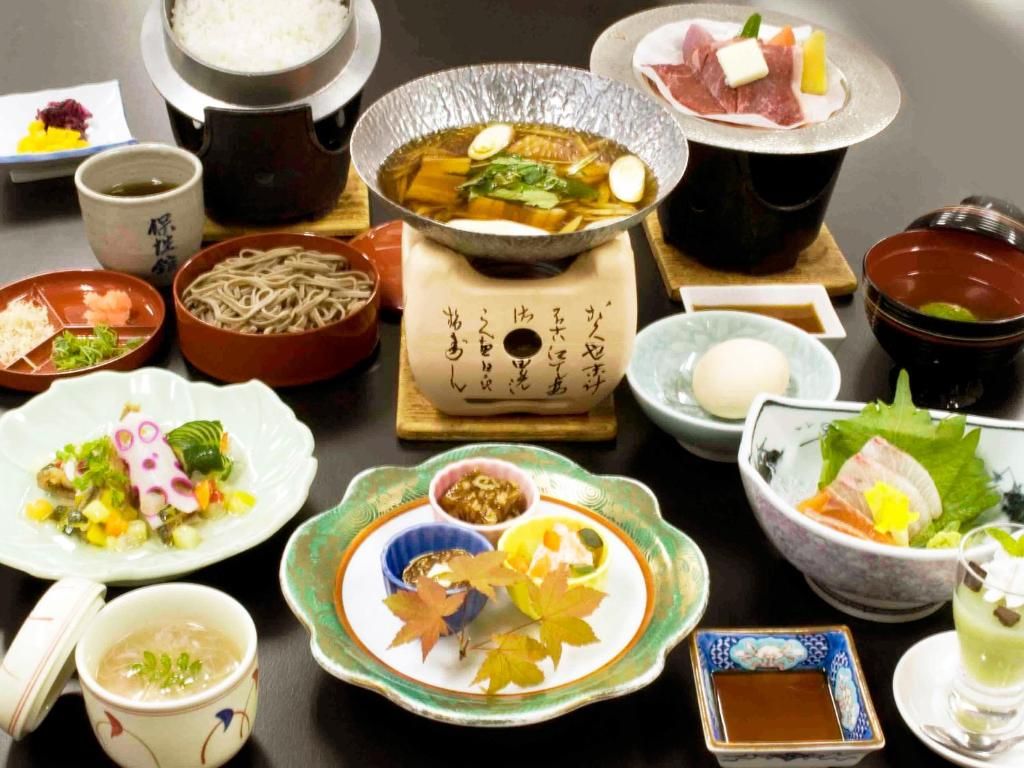 Un assortiment de plats japonais, notamment un plat mijoté, des sashimis et divers accompagnements.