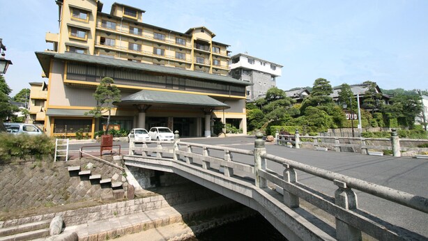 Un hôtel à plusieurs étages, doté d’une entrée imposante, d’un pont en pierre et d’un espace de stationnement.