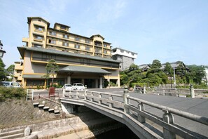 A multi-story hotel with a prominent entrance, a stone bridge, and a parking area. - Hoseikan (Matsue)