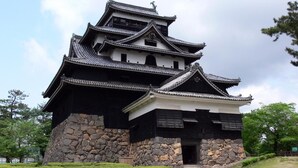Un château japonais traditionnel, à plusieurs niveaux et doté d’une base en pierre, entouré de haies bien entretenues.