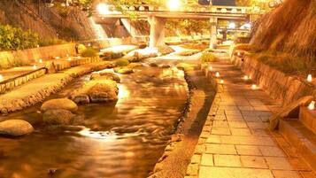 A nighttime riverside walkway with a bridge overhead, illuminated by street lamps.