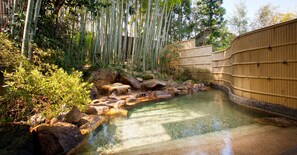 A serene outdoor pool area with bamboo walls, rocks, and lush greenery. - Ryotei Yamanoi (Matsue)